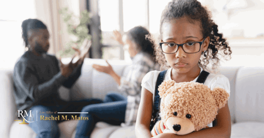 Child frowns and holds a teddy bear while parents argue in the background