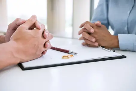 couple facing each other with divorce papers and wedding rings between them