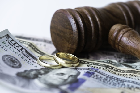 Judge gavel with wedding rings with $100 bills underneath